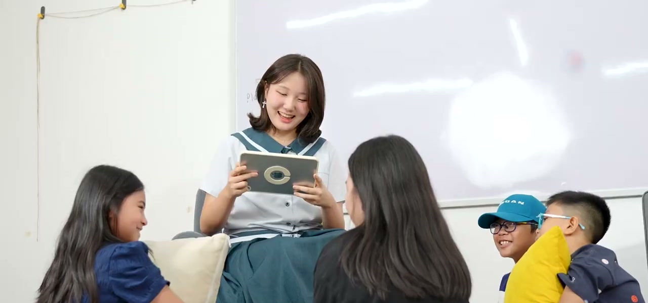 An older student reading from an iPad to younger children